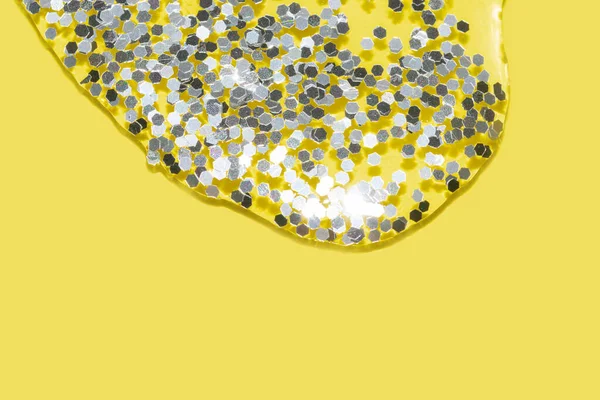 Transparent liquid with silver glitter pouring over a pastel yellow background — Stock Photo, Image