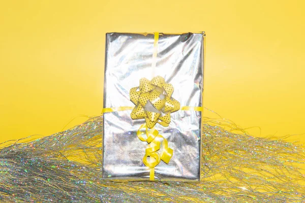 Regalo di Natale avvolto in lamina olografica d'argento con fiocco a nastro giallo — Foto Stock