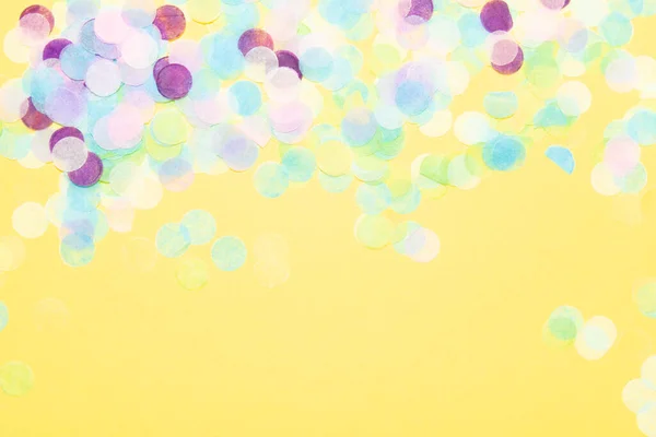 Papel azul, verde, roxo, rosa e amarelo confete sobre um fundo amarelo vibrante — Fotografia de Stock
