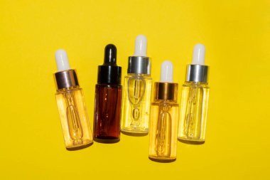 Güzellik serumu, hyaluronik asit ve sarı zemin üzerinde vitaminler olan farklı şişeler.