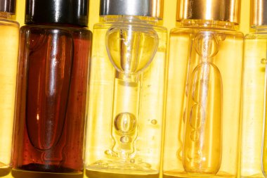 Güzellik serumu, hyaluronik asit ve sarı zemin üzerinde vitaminler olan farklı şişeler.