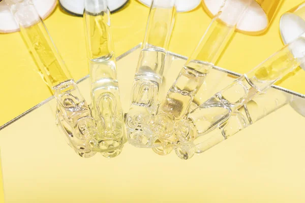 Conjunto de diferentes goteros de pipeta con suero, ácido hialurónico y vitaminas en un espejo sobre fondo amarillo — Foto de Stock
