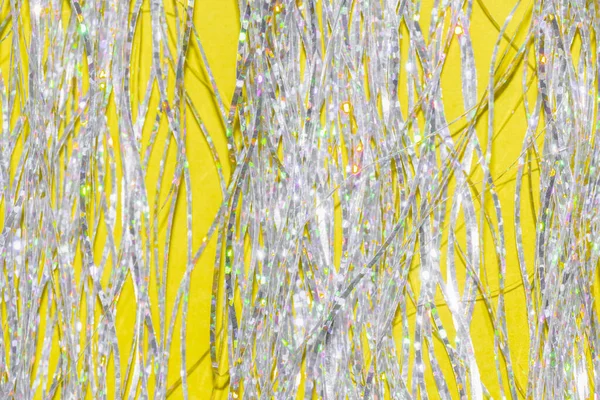 밝은 노란색 배경 위에 있는 은색 홀로그램 장식 술 — 스톡 사진