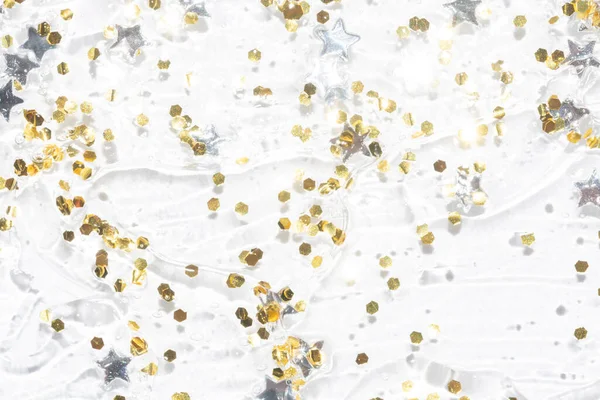 Brillo dorado y confeti estrella de plata en una textura de gel transparente —  Fotos de Stock