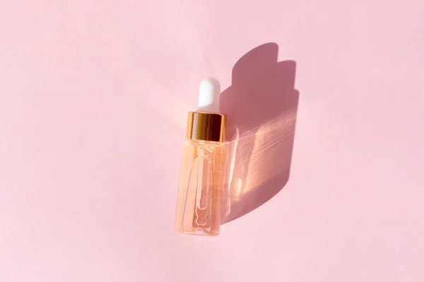 Suero de belleza de oro en una botella de pipeta sobre un fondo rosa — Foto de Stock