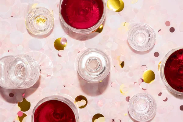 Flauti di champagne, bicchieri di vino e vodka su sfondo di coriandoli di carta rosa e oro — Foto Stock