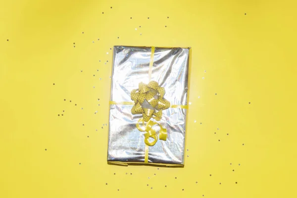Regalo de Navidad envuelto en papel holográfico plateado con lazo de cinta amarilla —  Fotos de Stock