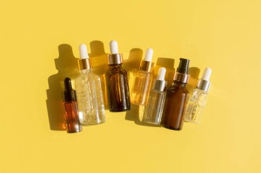 Güzellik serumu, hyaluronik asit ve sarı zemin üzerinde vitaminler olan farklı şişeler.