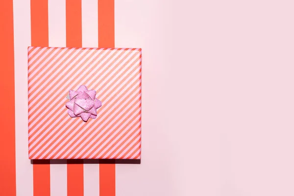 Scatola regalo di Natale a strisce rosa e rosse con un nastro su uno sfondo rosso rosa — Foto Stock