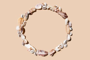 Bej bir zemin üzerinde deniz kabuklarından yapılmış yuvarlak çerçeve