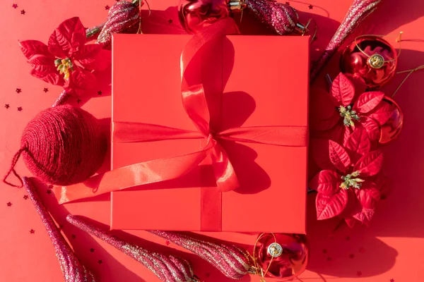 Confezione regalo di Natale rossa con poinsettia e ornamenti su sfondo rosso — Foto Stock