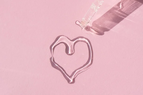 Primer plano de un gotero de pipeta con suero facial vertido en forma de corazón sobre un fondo rosa — Foto de Stock