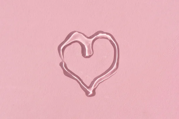 Verter suero facial en forma de corazón sobre un fondo rosa — Foto de Stock