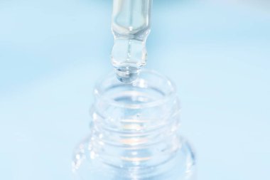 Mavi arka plandaki bir şişenin üzerine dökülen yüz serumunun ayrıntıları