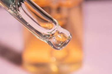 Pipet damlası makrosunu, cam şişeli pembe arka planda sıvı serumla kapatın.