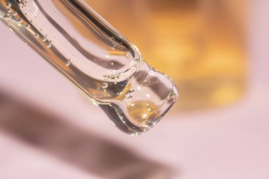 Pipet damlası makrosunu, cam şişeli pembe arka planda sıvı serumla kapatın.