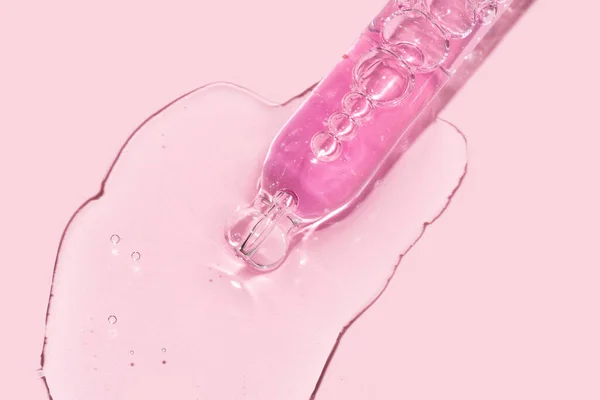 Pembe arka plana yüz serumu döken bir pipet damlatıcısını kapat.