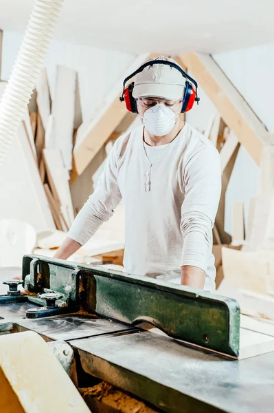 Carpintero trabajando cortando algunas tablas, lleva gafas de seguridad y protección auditiva — Foto de Stock