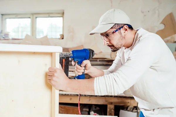 Charpentier travaillant à assembler un tiroir avec un tournevis, il porte des lunettes de protection — Photo