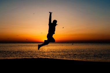 Havada kumsalda güneş doğarken atlama adam silüeti.