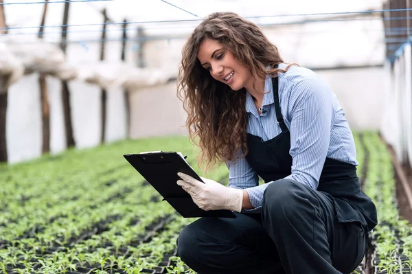 Biotechnology woman engineer with clipboard and pen, examining plants for disease — Stockfoto