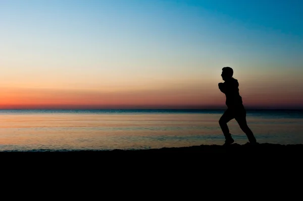 Silueta de hombre corriendo en la playa al amanecer — Foto de Stock