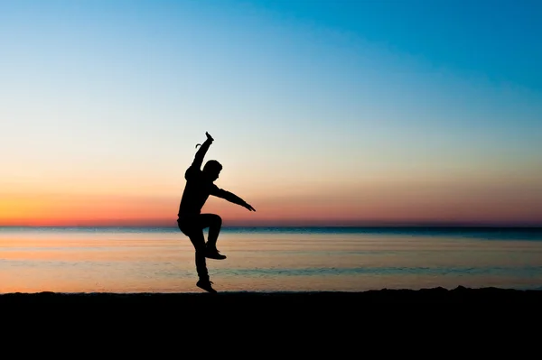 Silhouet van man springen in de lucht op het strand bij zonsopgang. — Stockfoto