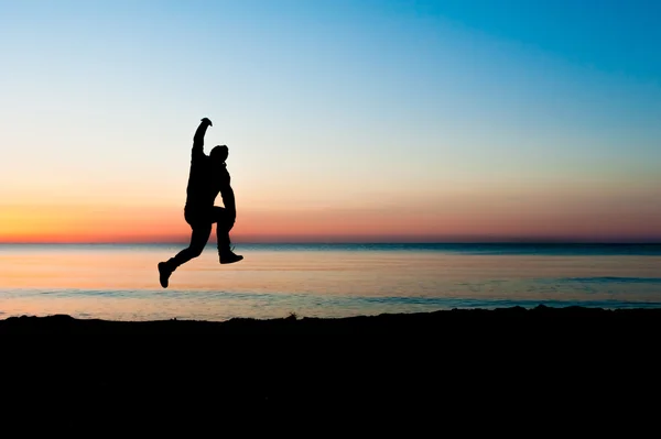 Silhouet van man springen in de lucht op het strand bij zonsopgang. — Stockfoto
