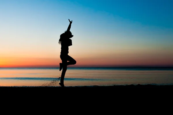 Silhouette of woman jumping in the air on the beach at sunrise.
