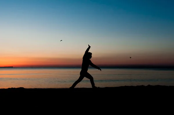 Silhouette of man jumping in the air on the beach at sunrise. — Stock Photo, Image