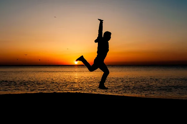 Silhouette of man jumping in the air on the beach at sunrise. — Stock Photo, Image