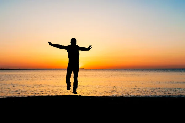 Silhouet van man springen in de lucht op het strand bij zonsopgang. — Stockfoto