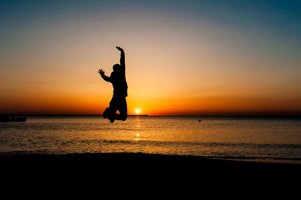 Silueta del hombre saltando en el aire en la playa al amanecer . — Foto de Stock