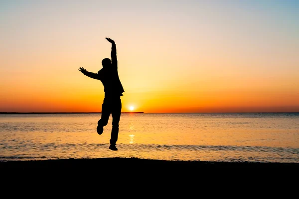 Silhouette of man jumping in the air on the beach at sunrise. — Stock Photo, Image