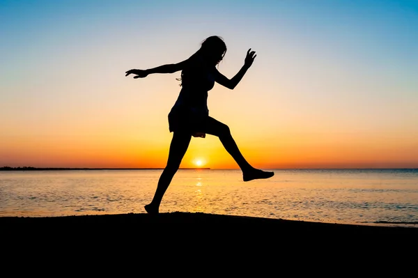 Silhouet van de vrouw springen in de lucht op het strand bij zonsopgang. — Stockfoto