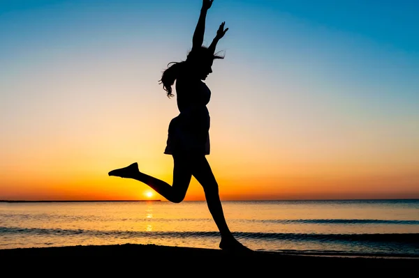 Silhouette of woman jumping in the air on the beach at sunrise. — Stock Photo, Image