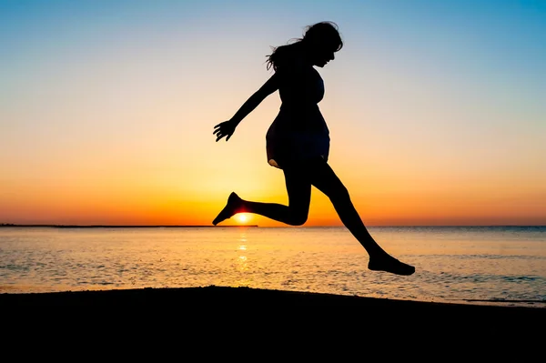 Silhouette of woman jumping in the air on the beach at sunrise. — Stock Photo, Image