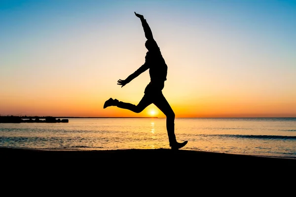 Silhouet van de vrouw springen in de lucht op het strand bij zonsopgang. — Stockfoto