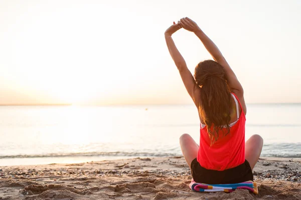 Jonge vrouw silhouet beoefenen van yoga op het strand bij zonsopgang. — Stockfoto