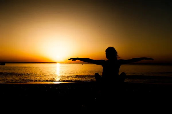 Sylwetka młoda kobieta praktykowania jogi na plaży w sunrise. — Zdjęcie stockowe