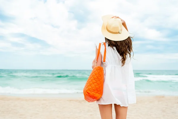 Woman in straw hat and white dress on a tropical beach with orange bag — Stock Photo, Image
