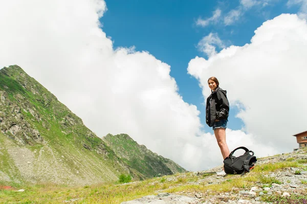 Young lady hiker with backpack sitting on mountain top admiring mountain landscape — Stock Photo, Image