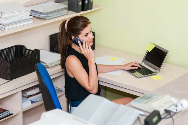 Jovem empresária sentada na mesa, conversando no celular . — Fotografia de Stock