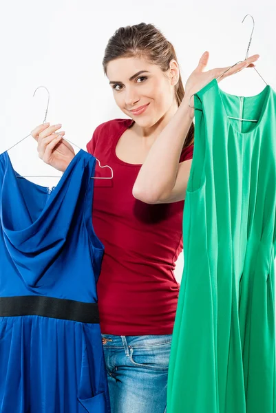 Beautiful brunette fashion model with a choice of dresses which she is holding up on hangers isolated on white — Stock Photo, Image