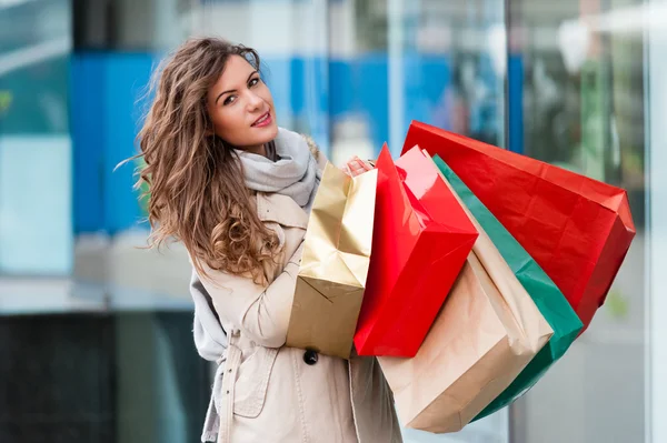 Foto de jovem mulher alegre com sacos de compras no fundo das janelas da loja — Fotografia de Stock