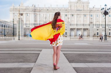 Young woman in front of Palacio de Oriente - the Royal Palace of Madrid, holding a flag.
