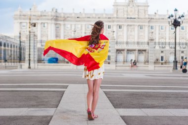 Young woman in front of Palacio de Oriente - the Royal Palace of Madrid, holding a flag.