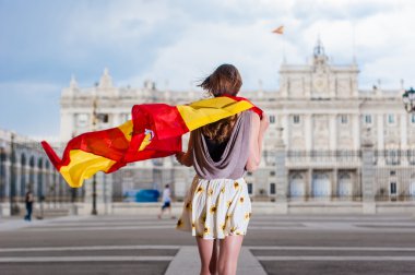 Young woman in front of Palacio de Oriente - the Royal Palace of Madrid, holding a flag.