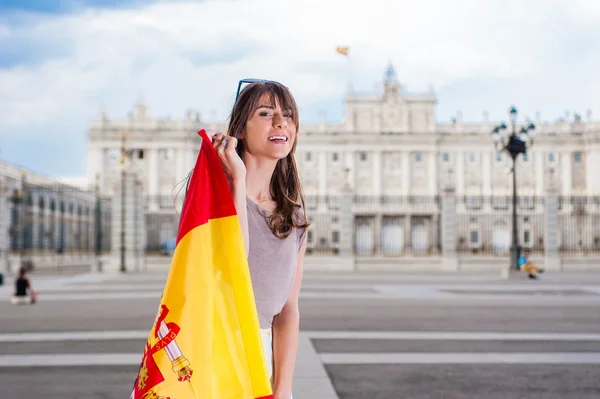 Jonge vrouw voor Palacio de Oriente - het Koninklijk Paleis van Madrid, houden een vlag met een grote glimlach. — Stockfoto