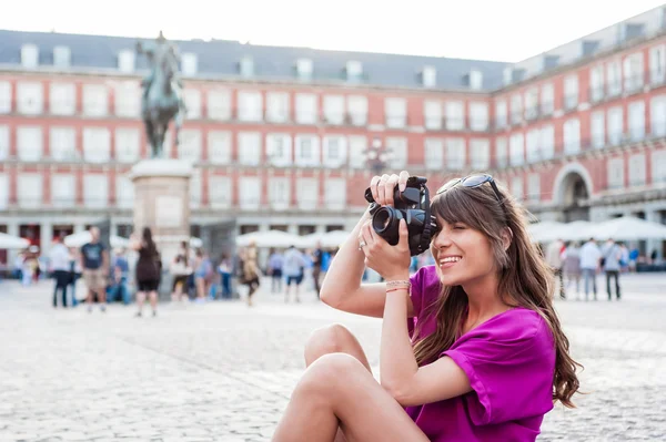 Young woman tourist holding a photo camera and taking picture in Plaza Mayor square, Madrid, Spain — Stock Photo, Image